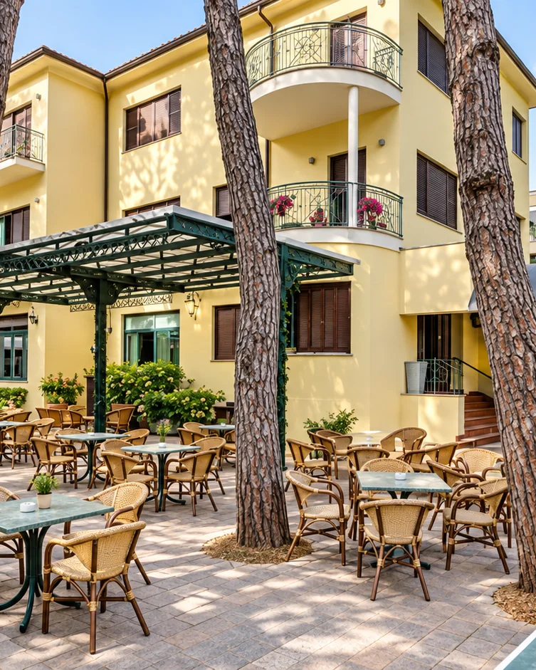 Hotel K2 at Cervia, a yellow three-storey hotel among umbrella pines, its garden terrace set with tables under a pergola