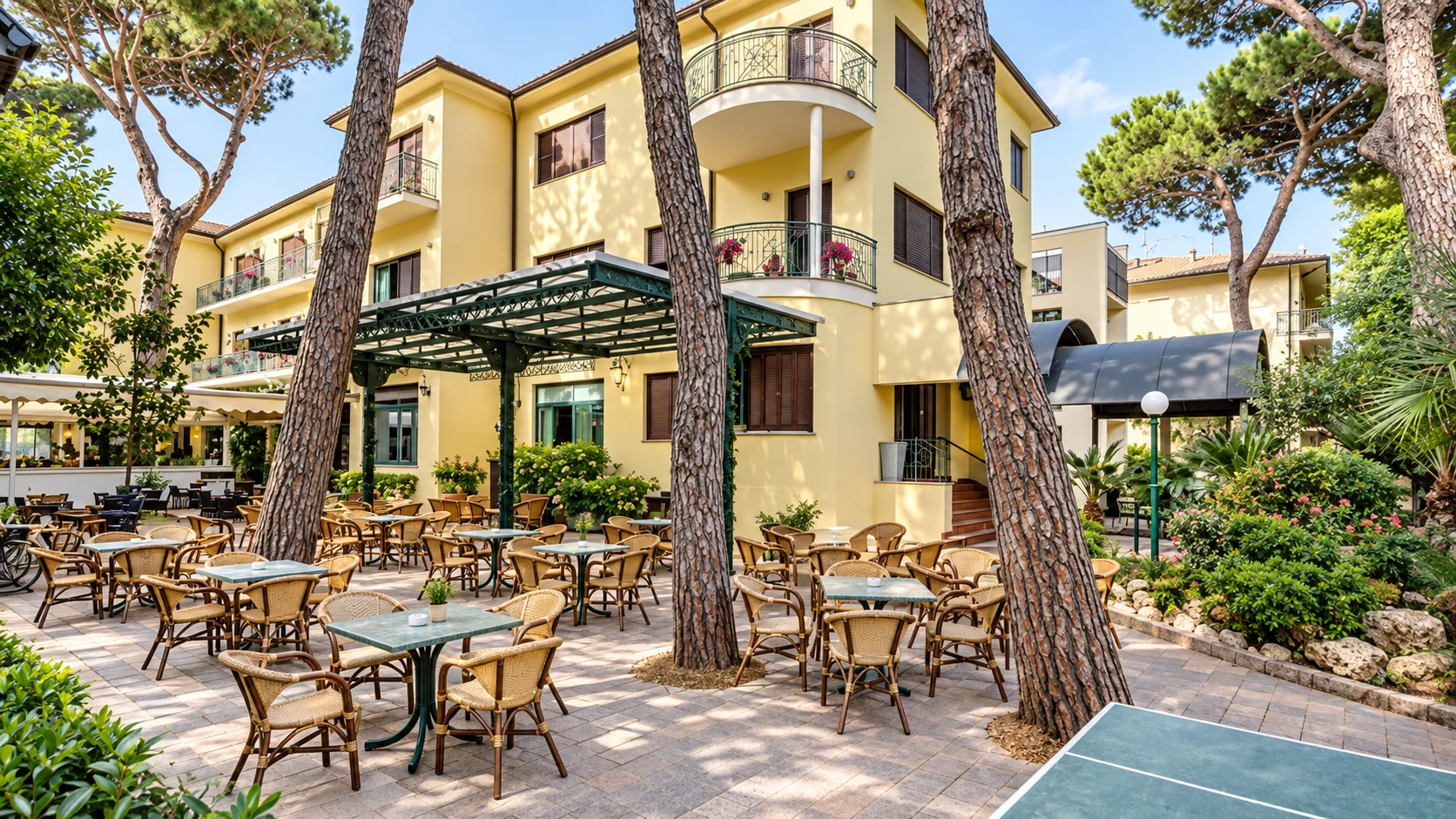 Hotel K2 at Cervia, a yellow three-storey hotel among umbrella pines, its garden terrace set with tables under a pergola