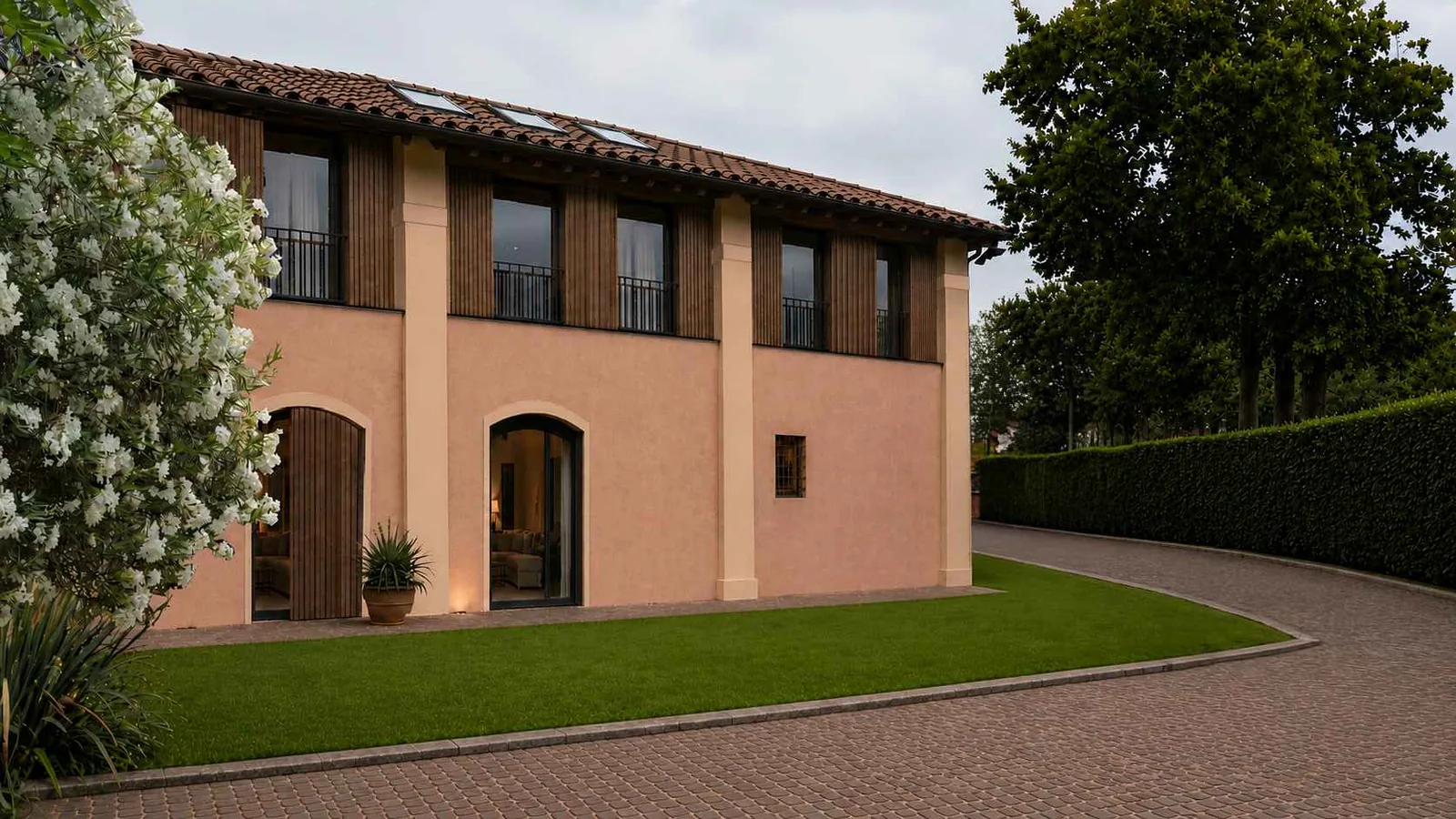 Building B from the garden: arched ground-floor openings with metal frames, timber-slatted upper windows with iron parapets, and a copper-edged tiled roof